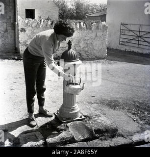 Donna bollitore di riempimento dal villaggio in ghisa pompa di stand la Gran Bretagna 1958 Foto Stock