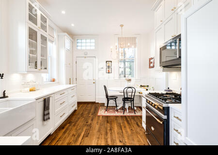 Una cucina bianca con una piccola sala da pranzo in un angolo e pavimenti in legno ovunque. Foto Stock