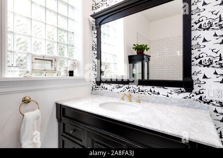 Un lussuoso bagno in un centro di Chicago in condominio con granito e oro hardware, legno scuro vanità e un accento parete con nero e sfondo bianco. Foto Stock