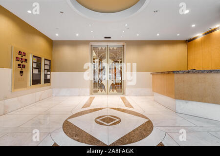 Area Frontale della lobby di un centro di Chicago alto edificio con pareti gialle, mattonelle di marmo e un oro fantasia porta che conduce agli ascensori. Foto Stock