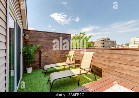 Un piccolo balcone sul tetto su un centro di Chicago in condominio con prato sedie a disposizione, turf sul terreno e un impianto nell'angolo circondato da pareti di legno. Foto Stock