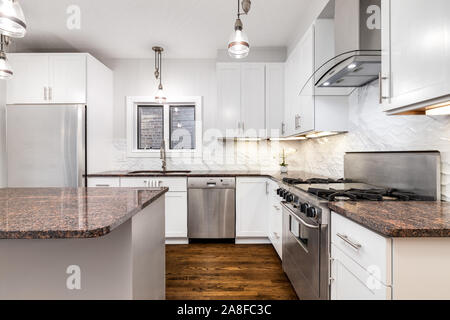 Un elegante e moderna cucina dotata di grigio e bianco screziato di granito, elettrodomestici di acciaio inossidabile, bianco armadi ed elettrodomestici di acciaio inossidabile. Foto Stock