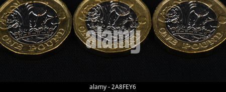 Chiudere fino a tre British pound monete in una riga su sfondo nero, web banner Dimensioni Foto Stock