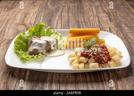 Gnocchi fatti in casa la pasta con la salsa di pomodoro e carne bovina mignon con salsa al formaggio in una piastra bianca su sfondo di legno Foto Stock