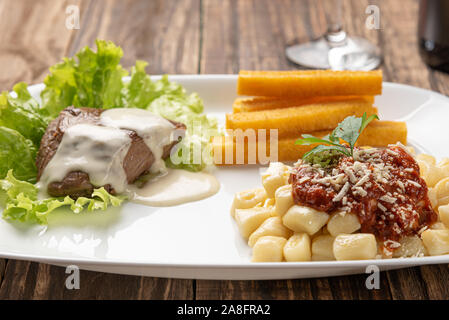 Gnocchi fatti in casa la pasta con la salsa di pomodoro e carne bovina mignon con salsa al formaggio in una piastra bianca su sfondo di legno Foto Stock