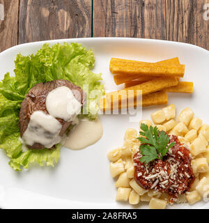 Gnocchi fatti in casa la pasta con la salsa di pomodoro e carne bovina mignon con salsa al formaggio in una piastra bianca su sfondo di legno Foto Stock