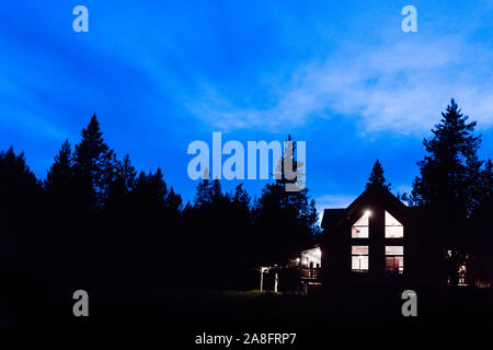 Rustico Lit log cabin in profondità nel bosco di notte tempo, subito dopo il tramonto, il profondo blu del cielo notturno Foto Stock