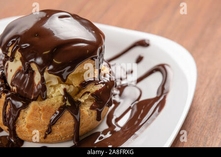 Profiteroles con gelato e cioccolato. Eclairs con cioccolato nero su sfondo di legno. Tradizionale Francese dessert. Foto Stock