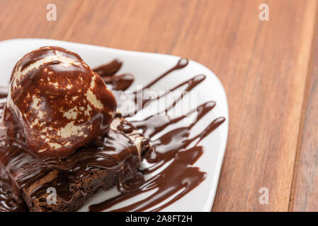 Brownie al cioccolato con gelato alla vaniglia e sciroppo di chocolatel isolato su sfondo di legno Foto Stock