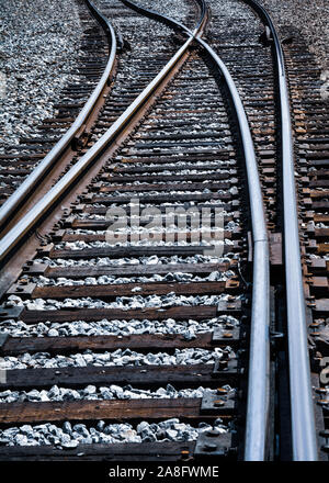 Una vista verso il basso di un treno via la curvatura e divergenti tra loro in corrispondenza di una forcella nelle piste di routing in un atmosfera isolata Foto Stock