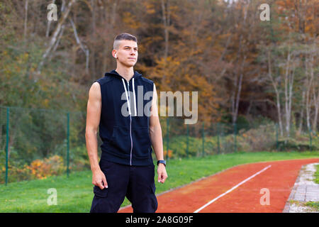 Ritratto di un giovane uomo del jogging al mattino all'esterno permanente sulla gara di corsa via Foto Stock