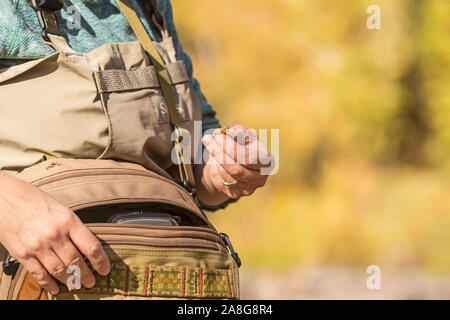 Una donna tira una vola fuori del suo hip pack su una soleggiata giornata di caduta lungo il fiume Poudre in Colorado. Foto Stock