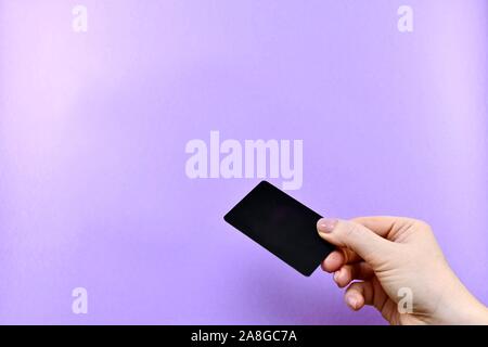 Dando un nero carta di credito o carta sconti con una mano su uno sfondo viola con lo spazio libero. Foto Stock