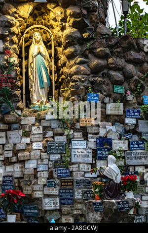 A Saigon, Vietnam, 18 dic. 2017, illuminata la statua della Vergine Maria nella popolare Ave Maria preghiera spot con muro di pietra piena di cartello, chiesa di Huy Foto Stock