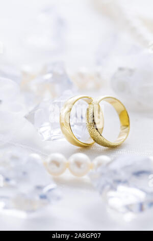 Due anelli d oro con collana di perle e su sfondo bianco come simbolo dell amore e del matrimonio Foto Stock