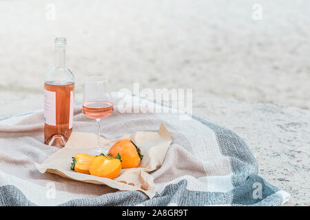 Picnic sulla spiaggia con kaki, mandorla e una bottiglia di vino rosato sulla coperta di colore beige. Foto Stock