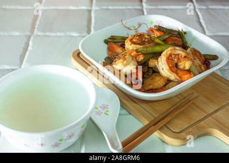 Stir-fried piccante di peperoncino essiccato francese di fagioli verdi con gamberi e una ciotola di porridge. Bacchette e cucchiaio. Il cibo sulla tavola. Foto Stock