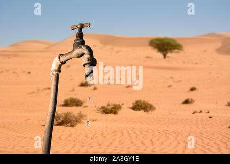 Rubinetto che gocciola e ambiente desertico in background, concetto di riscaldamento globale del pianeta e per la scarsità di acqua Foto Stock