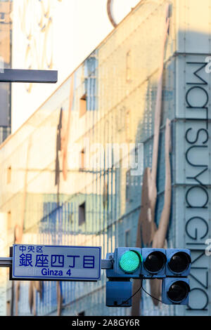 Compressi in prospettiva, al di fuori della messa a fuoco Matsuya Ginza department store con facciata in vetro verde. Focus sul primo piano Ginza 4 segno di traffico e di luce. Foto Stock