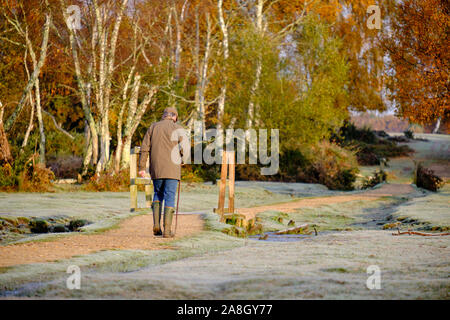 Brockenhurst, Hampshire, Regno Unito. 9 novembre 2019. In una gelida mattinata autunnale, la temperatura essendo immersa sotto il gelo durante la notte, l'attività abbonda in New Forest appena fuori di Brockenhurst. Uomo fuori per camminare presto sotto il sole freddo del mattino circa per attraversare piccolo ponte. Foto Stock