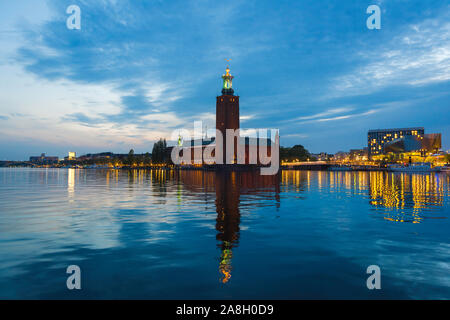 La città di Stoccolma, estate vista notturna attraverso il Riddarfjärden verso il Kungsholmen waterfront con City Hall (Stadshuset) edificio centro, Stoccolma. Foto Stock