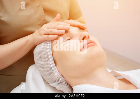 Massaggiatrice mani si muovono lentamente facendo rilassante massaggio viso alla bella ragazza client in Medical Center vista superiore Foto Stock