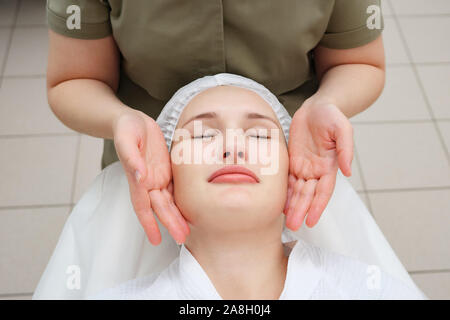 Massaggiatrice mani si muovono lentamente facendo rilassante massaggio viso alla bella ragazza client in Medical Center vista da sopra Foto Stock