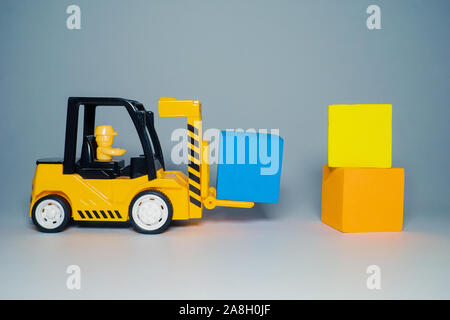 Giallo carrello carico giocattolo cubetti di colore. Giocattoli per bambini. Piccolo carrello caricatore e tre cubi Foto Stock