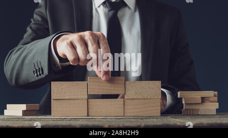 Vista frontale di un uomo d affari con la costruzione di una struttura di picchetti di legno in una immagine concettuale della visione aziendale e l'avvio. Foto Stock