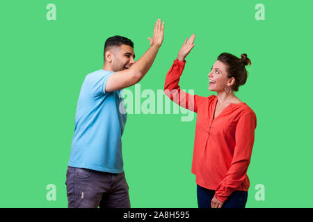 Vista laterale ritratto di entusiasti stupiti coppia giovane in abbigliamento casual in piedi dicendo ciao e dando alta cinque amici saluto ogni altro, lieto di soddisfare Foto Stock