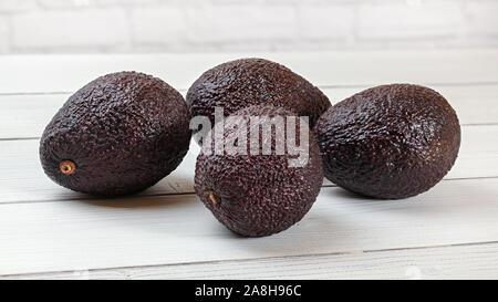 Il marrone scuro avocadi ( Bilse cultivar ) su lavagne bianche desk. Foto Stock