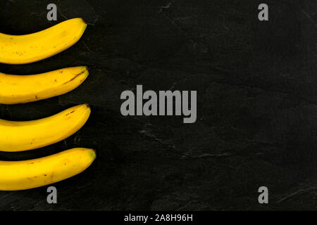 Quattro banane sul nero ardesia come board photo dal di sopra, solo parte di esse visibili, più spazio per il testo sul lato destro. Foto Stock