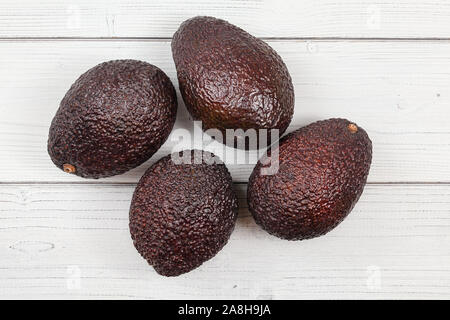 Vista del piano portapaziente, quattro marrone scuro avocado maturo ( bilse cultivar ) su lavagne bianche desk. Foto Stock