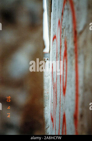 Michael Scott/Alamy Live News - Berlino, Germania Aprile 1990 - Un Oriente soldato tedesco può essere visto attraverso un buco nel muro di Berlino in aprile 1990 mesi dopo la caduta del muro di Berlino nel 1989. Foto Stock