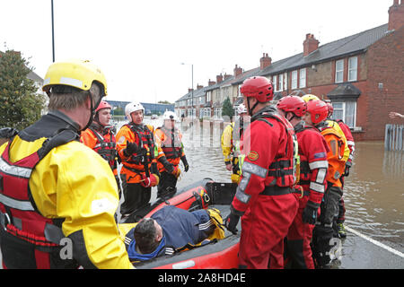 Servizi antincendio e di soccorso evacuare un uomo disabili dalla sua casa dopo le inondazioni nella zona di Bentley di Doncaster dopo mesi di pioggia cadde in un giorno caausing il fiume Don a violare le sue rive. Foto Stock