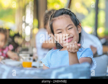 Bambino carina ragazza con un grande sorriso a tavola in un resort, cercando di fare qualche piccolo cuore. Messa a fuoco selezionata sul viso. Foto Stock