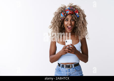 Sorpreso e divertito bella bionda moderna curly-pelose hipster girl, affannosa e mascella caduta da stupore vedere la persona famosa, registrare video Foto Stock