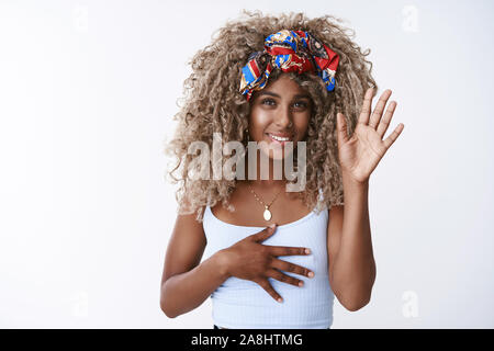 Ragazza giura ella onesti. Bella, elegante AFRICAN-AMERICAN curly-dai capelli donna bionda nella trendy hipster con archetto superiore, di alzare la mano e mettere sul cuore come Foto Stock