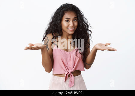 Colpevole carino scomodo afro-americano a ricciolo femmina dai capelli rosa in alto ritagliata, scrollare mani si sviluppa lateralmente, scusandosi per errore, sorridente Foto Stock