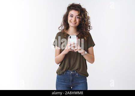 Ragazza tenendo la tua foto. Amichevole-cercando giovani carina ragazza, curly-haired dello smartphone di contenimento verticale di cattura fotografia sorridente largamente fotocamera Foto Stock