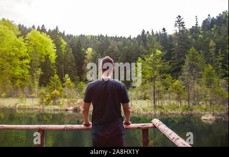 Solo l'uomo in piedi e guardando sul desolato lago nella foresta. Nozione di viaggio, psicologia, mindfulness. Foto Stock