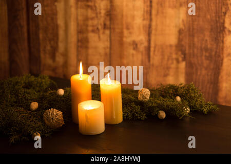 La minima nozione di Natale: tre candela accesa al buio su un tavolo di legno e legno rustico ambiente con rami di pino bianco e decorazioni naturali Foto Stock