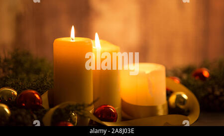 Il calore del concetto di Natale: close up di tre candele accese al buio su un tavolo in legno e con rami di pino, naturale pigne e oro e rosso Foto Stock