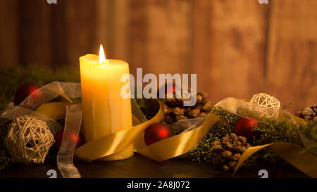 Il calore del concetto di Natale: close up di tre candele accese al buio su un tavolo in legno e con rami di pino, naturale pigne e oro e rosso Foto Stock