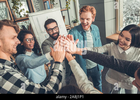 Startupers lavorando in ufficio insieme in piedi dando alta cinque top view felice Foto Stock