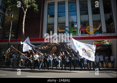 Un gruppo di ballerini con bandiere e membri dell'orchestra sono visti di fronte alla facciata del teatro come essi rappresentano per i media durante una parata promozionali di 'un Chorus Line' musical diretto dallo spagnolo attore e regista Antonio Banderas, precedendo la premiere al Soho Caixabank teatro il 15 novembre 2019. 'Un Chorus Line" è il nuovo musical di Antonio Banderas circa un gruppo di danzatori provenienti da Broadway che fanno parte di un coro musicale. Foto Stock