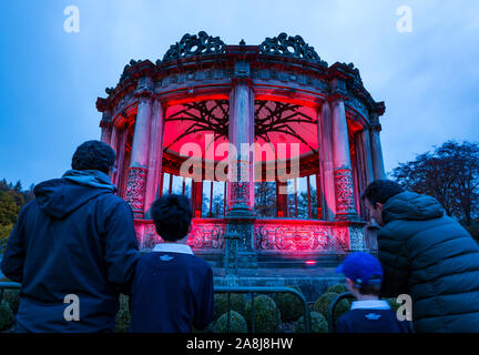 Dalkeith Country Park, Dalkeith, Midlothian, Scotland, Regno Unito, 9 novembre 2019. Papavero scozzese appello: Il Papavero Scozia illuminazione di campagna Red ha più di 120 edifici e strutture in tutta la Scozia illuminato in rosso nella settimana in esecuzione fino al Giorno del Ricordo. Gli ornati rovinato Orangerie è illuminato in rosso come l'oscurità cade. L'Orangery dispone di dodici lati con colonne doriche. Nella foto: Angus, Sam, Finn & Barry ammirare la struttura Foto Stock