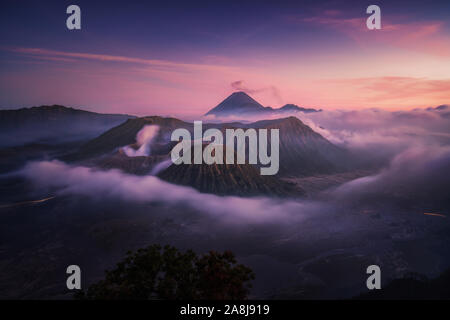 Monte Bromo al tramonto. Nebbia nella caldera, Semeru, e nube di cenere. Isola di Giava. Indonesia viaggio avventura. Foto Stock