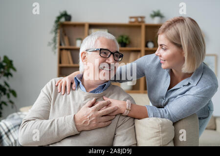 Senior riposante uomo sul divano guardando al suo giovane figlia in piedi vicino da Foto Stock