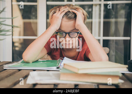 Stanco studente facendo i compiti a casa seduti all'aperto con i libri di scuola e giornale. Ragazzo stanco a causa delle pesanti studio. Bambino addormentato sul copybook dopo l Foto Stock